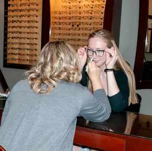 A woman with glasses is having her glasses adjusted by another woman in a store.