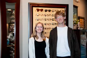 A young man and woman stand together in front of a display of glasses in a shop.