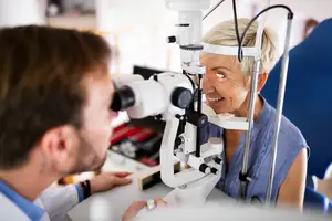 An optometrist examines a female patient's eyes with an ophthalmoscope in a clinic setting