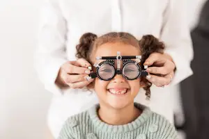 A young girl is being examined by an eye doctor wearing a pair of glasses and a green sweater.