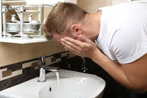A man washing his face with water from the sink faucet