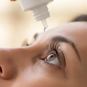 A woman is applying eye drops into her right eye.