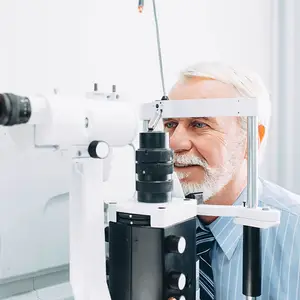 A senior man looking into an eye exam machine with his right eye.