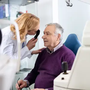 A doctor examining a patient's eye in a clinic with a blue chair in the background