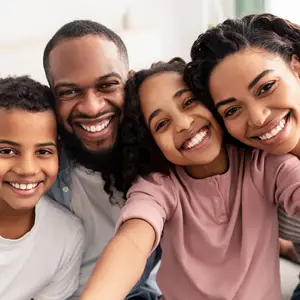 A smiling family, consisting of a man, a woman, and two kids, is probably taking a selfie together in a room.