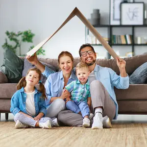 A family of four sitting on a couch with a cardboard house above them