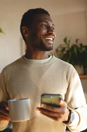 a man smiling while holding a cup and a cell phone