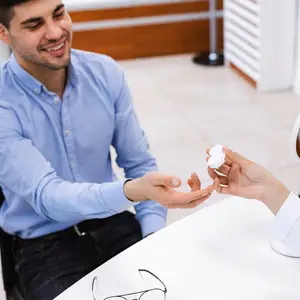A man is handing a contact lens to a woman who is probably a doctor in an optical shop.