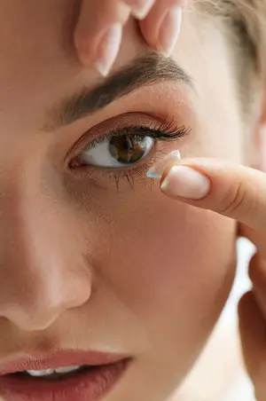 Close-up of a woman's face with a contact lens being placed on her eye.