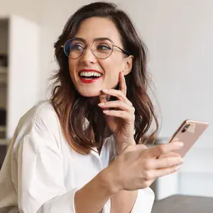 A woman wearing glasses and a white shirt smiling and looking at her phone