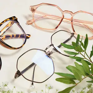A pair of glasses and three different glasses frames are placed on a white surface with green leaves and small white flowers. The glasses frames have different colors and designs, and the glasses have clear lenses. The frames are placed in a way that they are slightly overlapping each other. The glasses are placed in front of the frames. The leaves and flowers are placed on the right side of the glasses and frames.