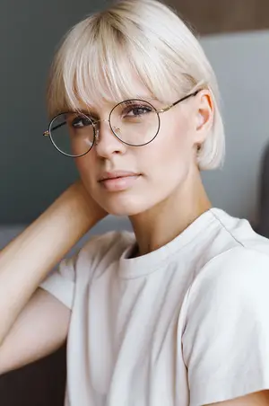 A woman wearing glasses is posing for a photo with her hand on her head.