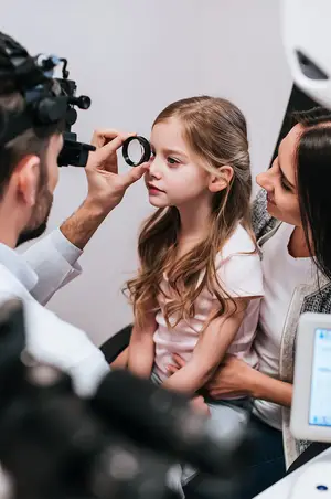 A young girl is being examined by a doctor using a magnifying glass and a ophthalmoscope.
