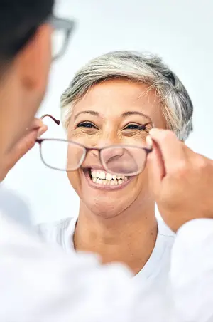 Woman adjusting glasses with a doctor examining her vision