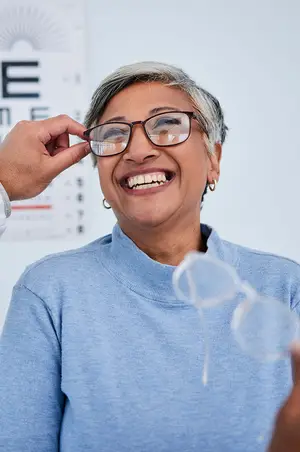 An older woman is smiling while trying on her glasses in a clinic.
