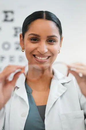 a woman wearing a white coat is smiling and holding a pair of eyeglasses