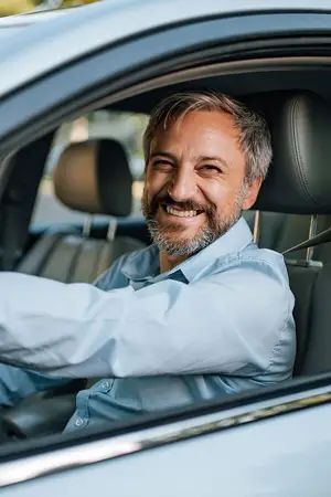 A smiling man in a blue shirt drives a car with a blurry background