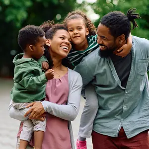 A happy family of four with two children, a girl and a boy, smiling and laughing in an outdoor setting.