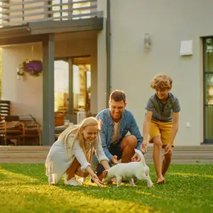 A family of three playing with a white puppy on the lawn in front of a modern house.