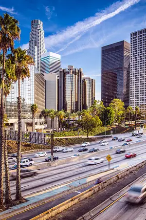 A city view with multiple high-rise buildings, cars, and trees during the daytime.