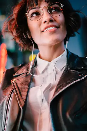A woman with short hair wearing a leather jacket and glasses is smiling and posing for a photo.