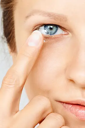 A woman is putting a contact lens in her eye.