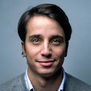 man smiling and wearing a gray sweater and blue shirt