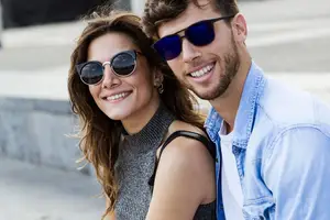 A man and a woman are standing together outside wearing sunglasses and smiling