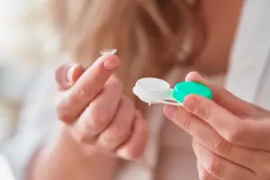 Woman holding a contact lens in her hand and looking at it.