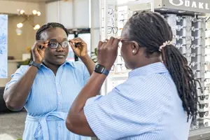 Two women in blue shirts look at each other in front of an Oakley display case