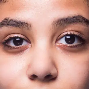 Close-up of a person's face with brown eyes, black eyelashes, and a slightly raised eyebrow