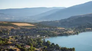 A top-down view of a lake with mountains and houses in the background during the daytime