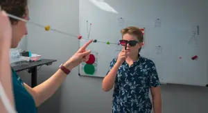 A woman is teaching a boy to use a stick with a colorful bead in front of a whiteboard