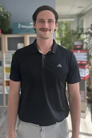 A smiling man in a black Adidas polo shirt and khaki pants standing in an indoor space.