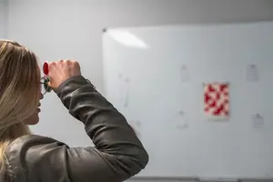 a woman holding a glass up to her face while looking at a white board