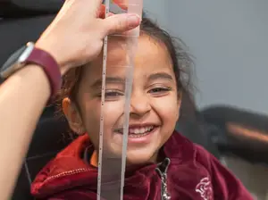 A young girl with a red jacket smiles at the camera while getting her height measured in a clinic.