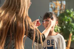 A woman is adjusting the glasses of a child in a room with sunlight coming through a window