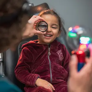 A young girl is smiling as a person holds a magnifying glass up to her face in a dental office.