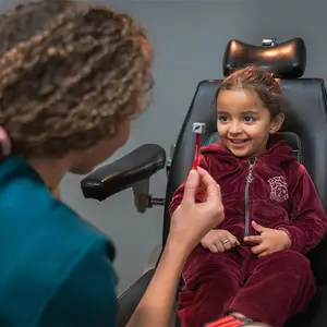 A girl with a tooth stick and a woman wearing blue is in a dental chair