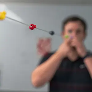 A man wearing a black shirt is playing a musical instrument with a stick in his hand in a classroom.