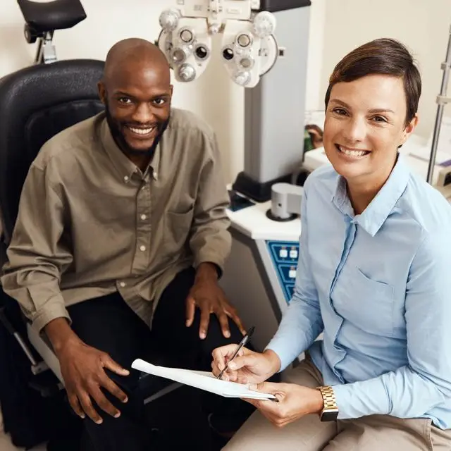African American male patient smiling and looking at an optometrist while holding a paper and a pen