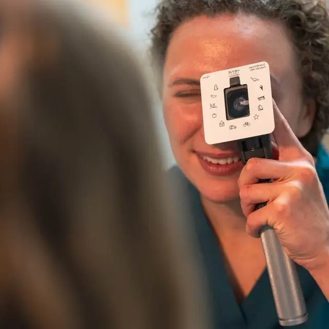A woman is holding a ophthalmoscope with a printed scale in front of her eye.