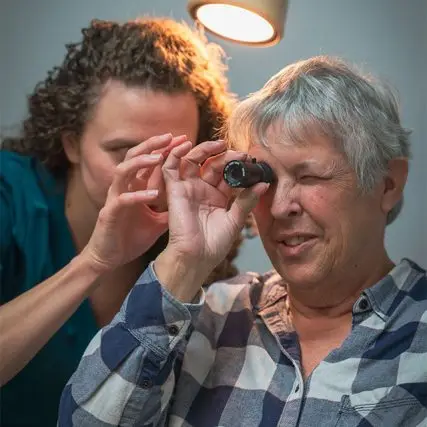 An older woman has her eyes examined by an optometrist with a magnifying device