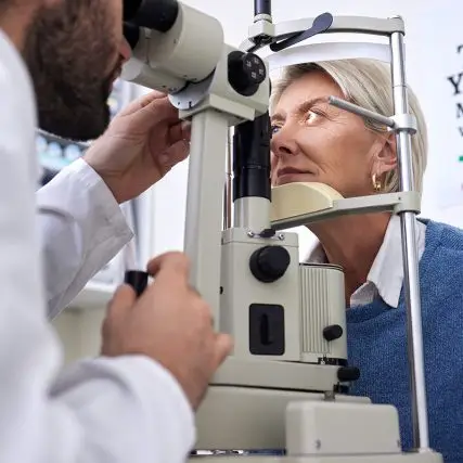 An eye doctor examining a patient's eyes with a slit lamp in a clinic.
