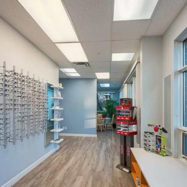 A room with wooden floors, a white ceiling, and a wall display of glasses in a store.