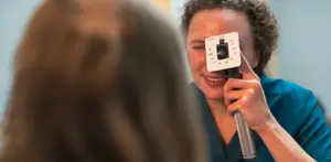An eye doctor is examining the patient's eyes with a device in her hand.