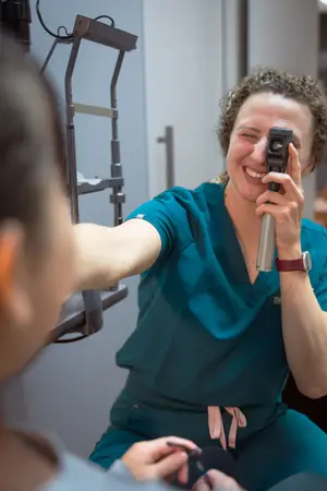 A woman with a watch and a smiling face is using a device to check the eyes of another person