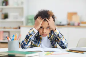 A boy sitting in front of a table with his head in his hands and a book in front of him