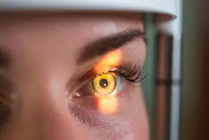 Close up of a woman's face with an eye in focus, illuminated by a light source, possibly a doctor's office or a beauty clinic