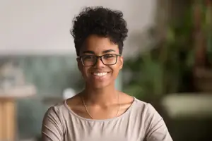 A woman wearing glasses and smiling at the camera inside an office.